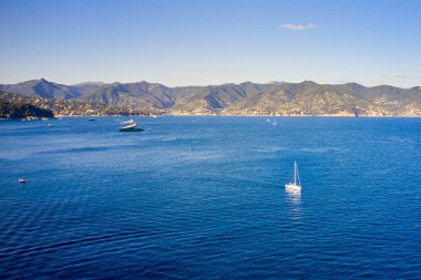 Yat, dağ zemininde parlak mavi suyla denizde yüzüyor. Ligurian Denizi 'nde tekne, Portofino, İtalya