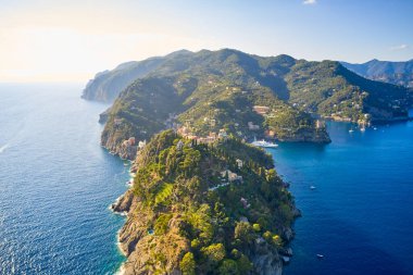 Dağlık alanda Arial manzaralı, önü Ligurian Denizi 'ne yakın beyaz bir deniz feneri var. Geleneksel İtalyan evleri tepenin üstünde yer alır.