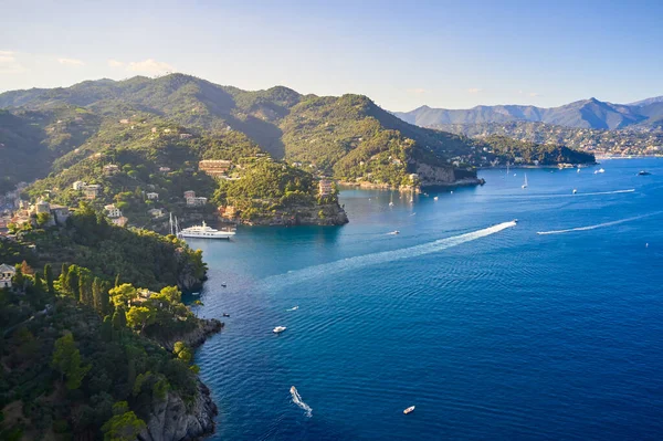 Yatlar ve tekneler İtalya 'nın Portofino kentindeki dağlık arka planda Ligurian Denizi' nde yol alıyorlar. Üzerinde geleneksel İtalyan evleri olan kayalar ve tepeler..