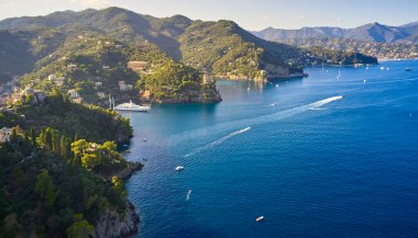 Yatlar ve tekneler İtalya 'nın Portofino kentindeki dağlık arka planda Ligurian Denizi' nde yol alıyorlar. Üzerinde geleneksel İtalyan evleri olan kayalar ve tepeler.