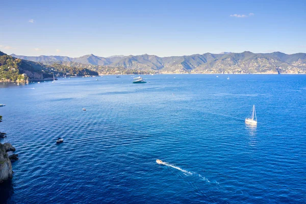 Yat, dağ zemininde parlak mavi suyla denizde yüzüyor. Ligurian Denizi 'nde tekne, Portofino, İtalya