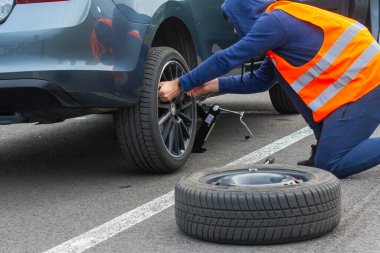 Turuncu güvenlik yeleği giyen bir adam yolda lastiği patlatır. Kapanış adamı elleri bozuk bir arabanın direksiyonuna dayanıyor. Prag, Mart 2020 'de Skrewdriver kullanılarak tekerleğin değiştirilmesi.