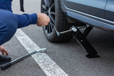 Patlak lastiğin tamiri yakın mesafede. Adam direksiyon değiştirmek için kriko kullanarak araba kaldırıyor. Kış ve yaz lastikleri değiştiriliyor. Mevsimlik lastik değiştirme konsepti. Prag, Mart 2020