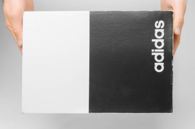 Beyaz arka planda Adidas kutusunu tutan adamların ellerini kapat. Adamın elinde Adidas logosu olan siyah beyaz bir kutu var, San Francisco, ABD, Mart 2020.
