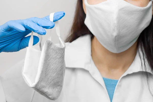 Protect yourself using a medicine mask. Woman is holding a respirator mask protective from virus infection, pandemic during quarantine. Doctor in a white coat and protective gloves. Concept of self protection