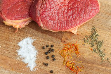 Çiğ et dilimlerinin en üst görüntüsü ahşap bir masaüstünde, biber, safran ve biberiyeli. Lezzetli yemek kavramı. Biftek pişirmek için gerekli malzemeler.