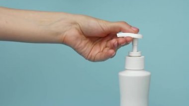 Yakın plan kadın, mavi arka planda Coronavirus 'a karşı korunmak için şişeye sıvı sabunla bastırıyor ve ellerini yıkıyor..