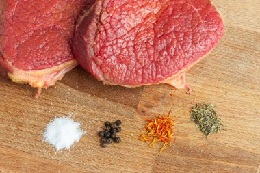 Çiğ et dilimlerinin en üst görüntüsü ahşap masaüstü üzerinde biber, safran, biberiye ve tuz bulunur. Sağlıklı akşam yemeği kavramı. Biftek pişirmek için gerekli malzemeler.