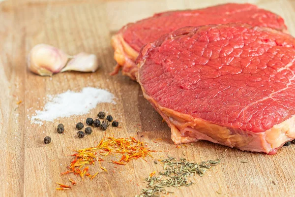 Carne cruda en una mesa de madera con ajo, sal, pimienta negra, azafrán y romero listo para cocinar . —  Fotos de Stock