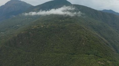 Dağların tepesindeki ağaçların yeşil tepeleriyle panoramik manzara. Bulutlar bir tepenin üzerinden uçuyor, İtalya