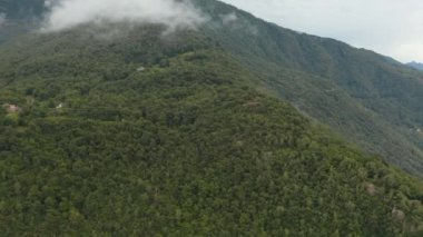 Dağların tepesindeki ağaçların yeşil tepeleriyle panoramik manzara. Bulutlar bir tepenin üzerinden uçuyor, İtalya