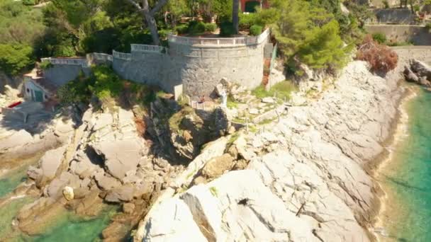 Fliegen Sie um eine weiße Jesus-Statue auf dem felsigen Hügel im Ligurischen Meer. Ein Strand mit Festungsmauer wird von türkisblaugrünem Wasser umspült, Camogli, Italien, April 2020 — Stockvideo