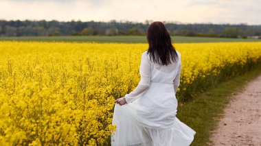 Sarı kolza tohumu çiçekleri içinde dönen beyaz elbiseli genç bir kadın. Fotokopi çekilen düğün fotoğrafları. Hayatın tadını çıkarıyorum.