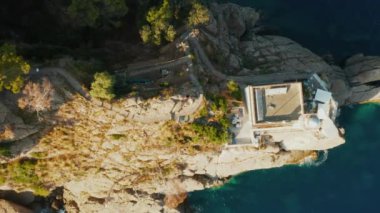 İtalya 'nın Portofino kentindeki bir deniz fenerinin üzerinden yaklaşan hava manzarası. Ligurian Denizi 'nin mavi suyuyla çevrili kayalık bir tepede bir deniz feneri var.. 