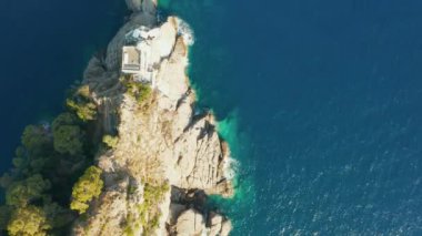 Ligurian Denizi 'ndeki kayalık bir tepenin üzerinde mavi turkuaz su ve dipte kocaman taşlarla uçarken Portofino, İtalya. 