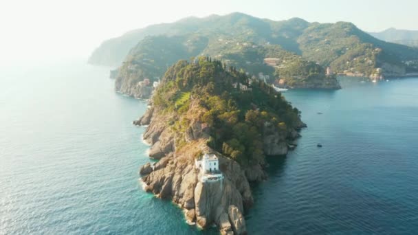 Flygbilder från en fyr med gröna träd och villor i Portofino, Italien. En kulle är omgiven av Liguriska havet med turkost vatten. — Stockvideo