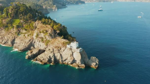 Flyger runt en fyr som står på en stenig kulle i Liguriska havet med blått turkost vatten och enorma stenar på en botten, Portofino, Italien. — Stockvideo