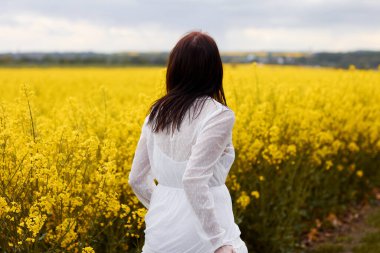 Beyaz elbiseli genç kadın kolza tohumu tarlası boyunca koşuyor. Kopya alanı ile başarı, ekoloji ve özgürlük kavramları.