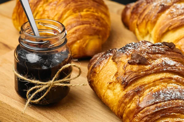 Croissant recentemente assado com um engarrafamento de baga em um jarro em uma mesa de madeira. Conceito de pequeno-almoço francês. Pastelaria caseira . — Fotografia de Stock