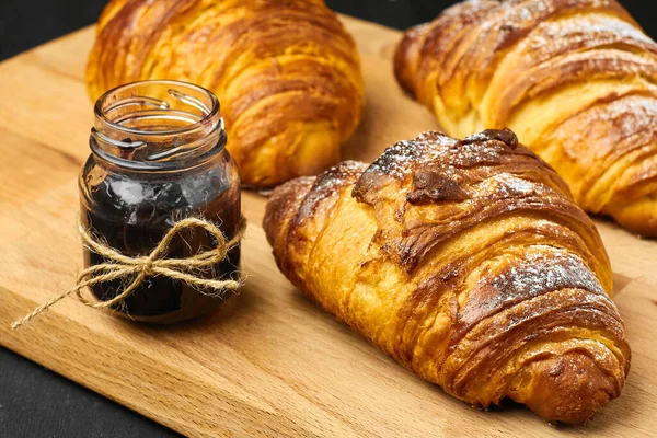 Croissant recentemente assado com um engarrafamento de baga em um jarro em uma mesa de madeira. Conceito de pequeno-almoço francês. Pastelaria caseira . — Fotografia de Stock