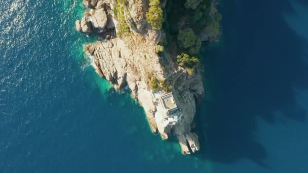 Flying over a lighthouse standing on a rocky hill in Ligurian sea with blue turquoise water and huge stones on a bottom, Portofino, Italy. Royalty Free Stock Video