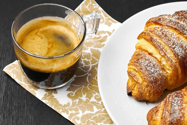 Eine Tasse Kaffee und frisch gebackene Croissants auf einem weißen Teller. Konzept des Imbisses. — Stockfoto