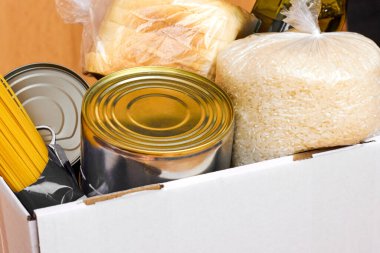 Tahta arka planda konserve yiyecek, makarna ve pirinç olan bağış kutusu. Yiyecek teslimatı ya da yardım konsepti