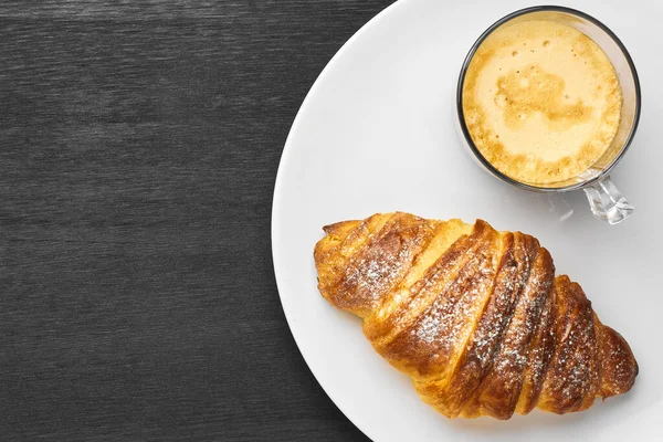 Cappuccino e croissant em uma chapa em um fundo preto com espaço de cópia. Conceito de um saboroso café da manhã. Pastelaria francesa ou italiana . — Fotografia de Stock