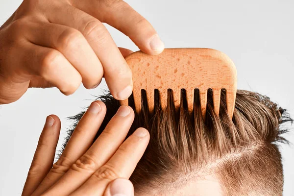 Молодий чоловік укладає волосся дерев'яним гребенем. Стилізація волосся в домашніх умовах. Рекламна концепція шампуню для здорового волосся та проти лупи . — стокове фото