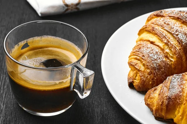 Une tasse de café, des croissants au beurre et une serviette en coton sur fond noir. Une idée de petit déjeuner . — Photo