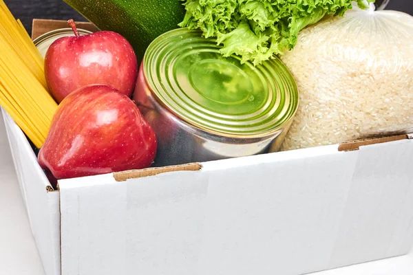 Donation box with vegetables, zucchini, salad, fruits, apples, olive oil, rice, pasta and tin on a wooden background