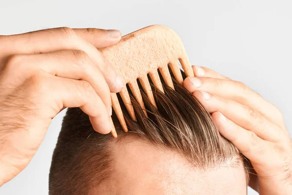 Young man styling his hair with a wooden comb. Hair styling at home. Advertising concept of shampoo for healthy hair and against dandruff. — Stock Photo, Image