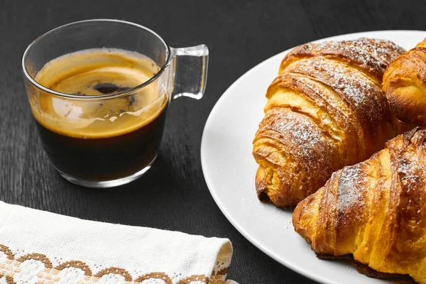 Une tasse de café, des croissants au beurre et une serviette de coton sur fond noir. Idée de petit déjeuner . — Photo