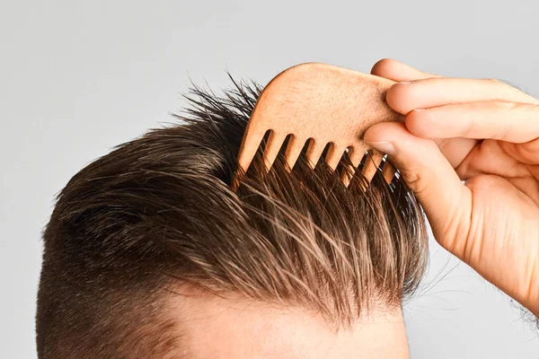 Mladý muž si upravoval vlasy dřevěným hřebenem. Styl vlasů doma. Reklamní koncept šampon na zdravé vlasy a proti lupům. — Stock fotografie