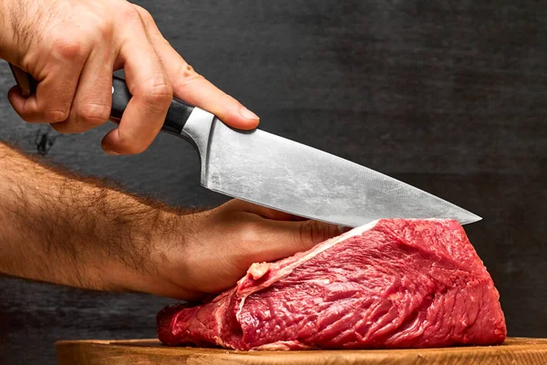 Primo piano uomo mano tagliando una carne di manzo con un coltello su uno sfondo nero. Concetto di farina proteica sana . — Foto Stock