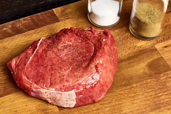 El pedazo fresco de la carne de vaca junto a las botellas de sal y pimienta en la tabla de madera. Concepto de recepción . —  Fotos de Stock