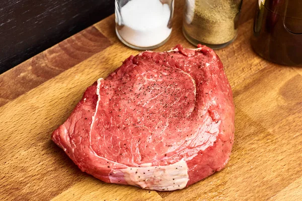 El pedazo fresco crudo de la carne de vaca junto a la sal y la pimienta en las botellas de cristal sobre el fondo negro. Concepto de recepción . —  Fotos de Stock