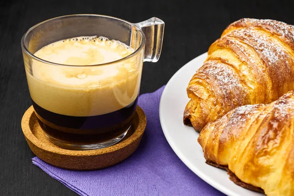 Schließen Sie eine Tasse Espresso und frische Croissants auf einer violetten Serviette. Konzept des Frühstücks auf schwarzem Hintergrund — Stockfoto