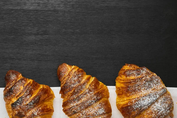 Top view of three croissants on a black background with copy space. Delivery of products — Stock Photo, Image