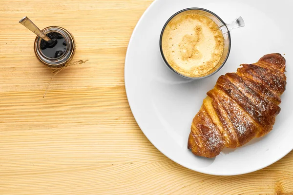 Vista superior em um café da manhã composto por uma xícara de café, um croissant com geléia em uma mesa de madeira com espaço de cópia — Fotografia de Stock