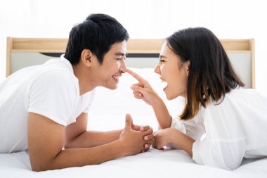 Yatak odasındaki komik ve romantik Asyalı çift portresi. Pencereden yansıyan doğal ışık, karı koca arasındaki ilişki ve aile olma kavramı..