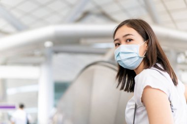 Kalabalık bir alışveriş merkezinde yürürken yüzüne hijyen koruyucu bir maske takan Asyalı genç bir kadın. Sağlık ve hastalık önleme Coronavirus, Covid19 gribi kalabalık bir yerde.