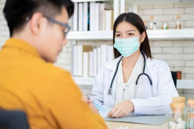 Asyalı uzman doktor hastanedeki bir hastayla konuşuyor. Hasta hastalığından ve gribinden endişeleniyor. Doktora gidip hastanede muayene oluyor. Sağlık hizmetleri kavramı.