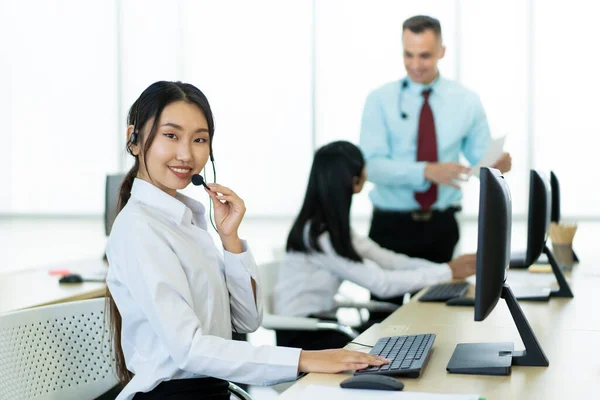 Smart young Asian and Caucasian ethnicity workers working in the office. Helpdesk and telemarketing sales representative team in working. Corporate call center team talking via using headset.