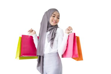 Kırpma yolu ile izole edilmiş. Asyalı genç Müslüman bir kadın elinde renkli kağıt poşetler tutuyor. Alışveriş konseptinde poz veren Müslüman kadın.