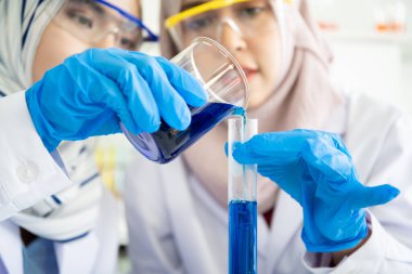 Asyalı genç Müslüman bilim adamı hastane laboratuvarında kimyasal deneyi test ediyor. Laboratuvarda araştırma yapan ve deney yapan profesyonel bir kimyager..