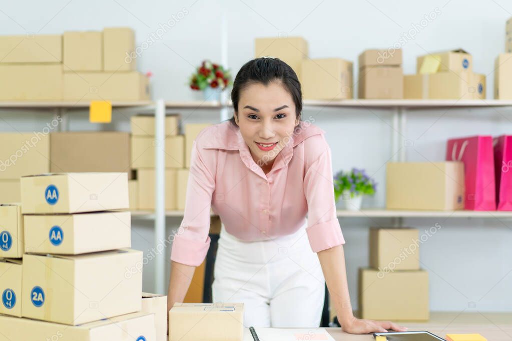 Beautiful young Asian woman online seller packing and checking for incoming orders in the warehouse. Young woman merchant selling products through online marketplace concept.