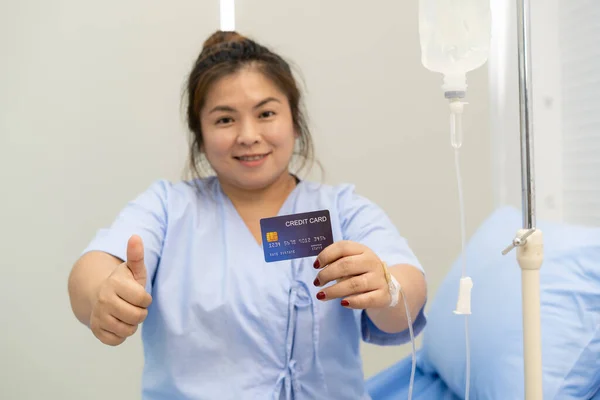 Asian fat woman stay in hospital and showing up a credit card with thumb up, financial support in medical and health care