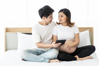 Romantik karı koca yatak odasındaki tableti kullanarak kaşlarını çatıyor ve internette bilgi topluyor. Hamile kadın ve koca için tatilde boş zaman aktivitesi. Birlikte hareket