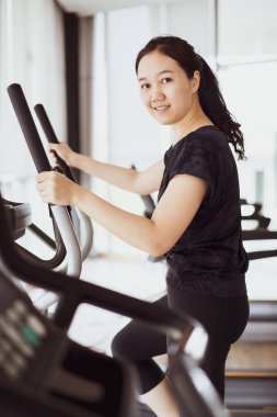 Genç atlet Asyalı kadın kapalı spor salonunda yoğun kardiyo egzersizi yapıyor. Kardiyo egzersizi için eliptik makine kullanan bir kadın. Sağlıklı ve sağlıklı olma kavramı.